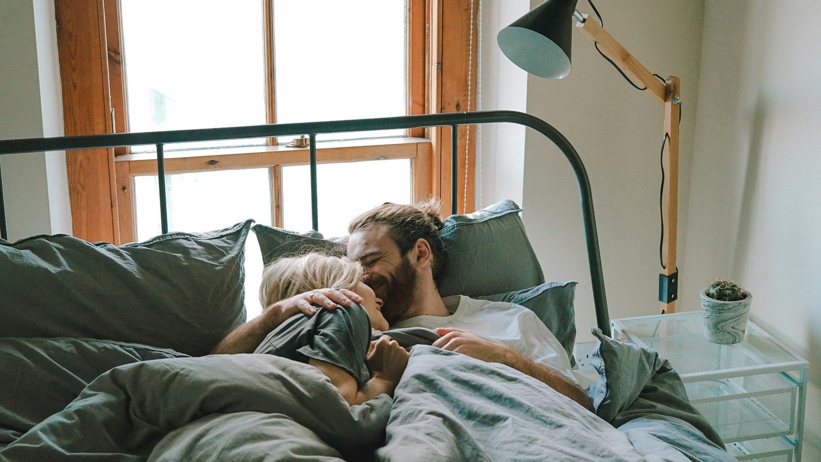 Pareja abrazada en la cama al despertar, ropa de cama gris, luz de mañana